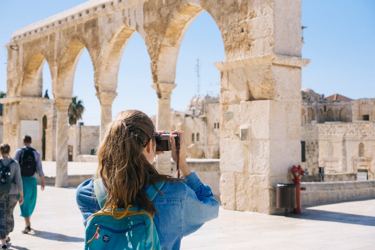digital A tourist photographs the ancient stone arches in Jerusalem's Old Town, capturing the essence of travel and history.