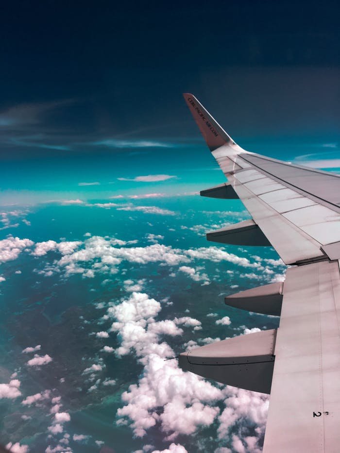 creative Aerial view of airplane wing over fluffy clouds with a deep turquoise sky.